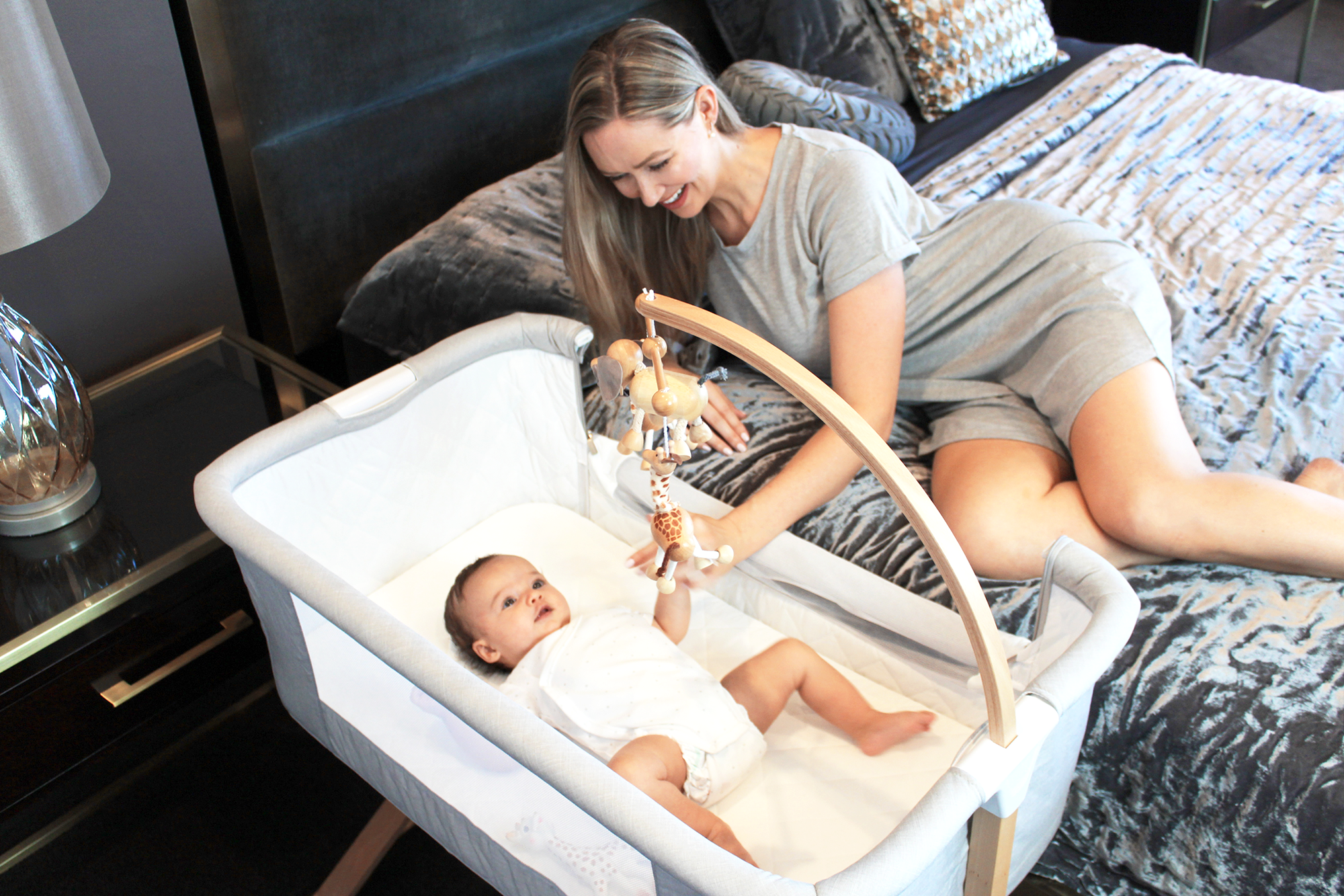 Smiling mother playing with baby in a bedside bassinet, Babyhood GCC bedroom setting