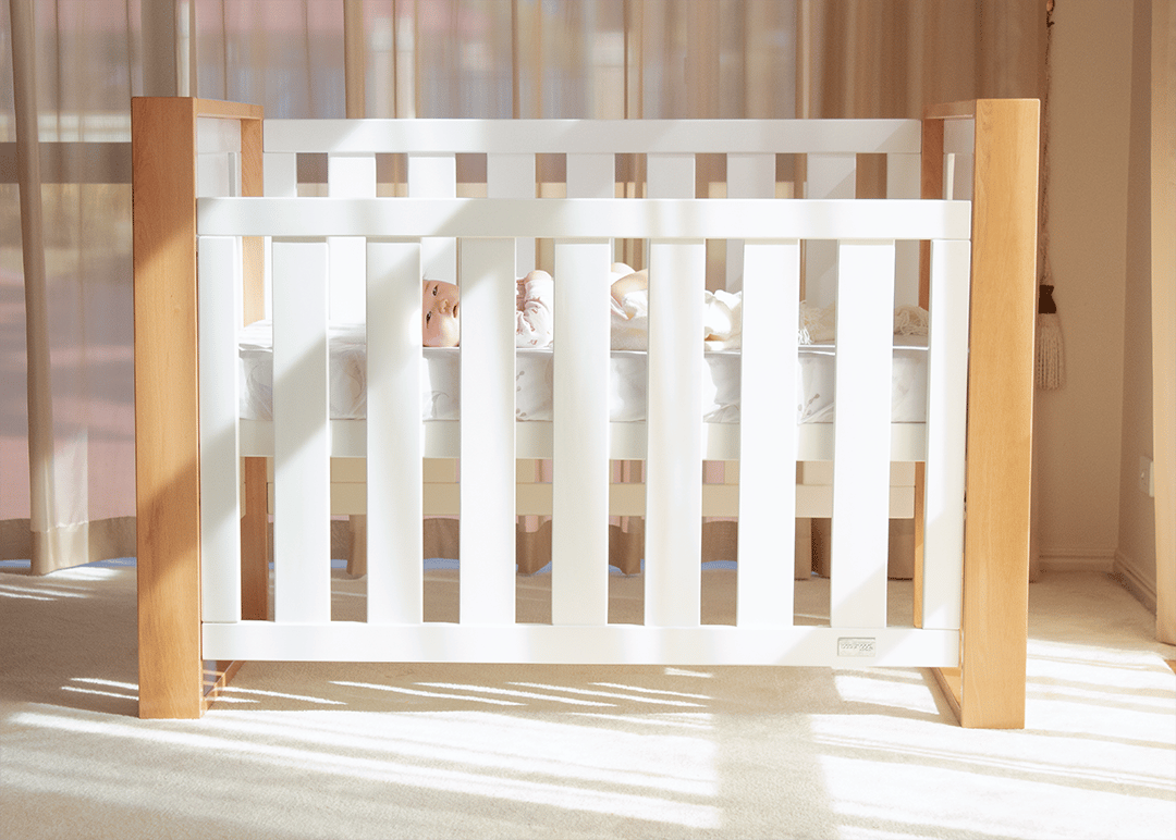 Baby lying in a modern white wooden crib in a sunlit nursery, Babyhood GCC