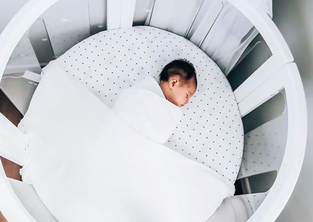 Newborn baby sleeping in a round white crib with dotted bedding, Babyhood GCC