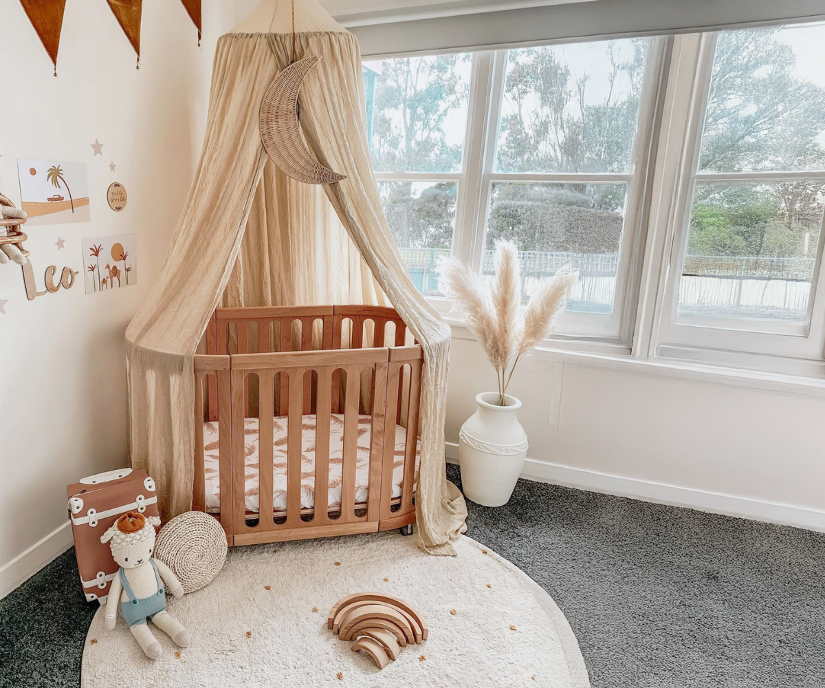 Modern baby nursery with wooden crib, beige canopy, plush doll, and decorative wall art
