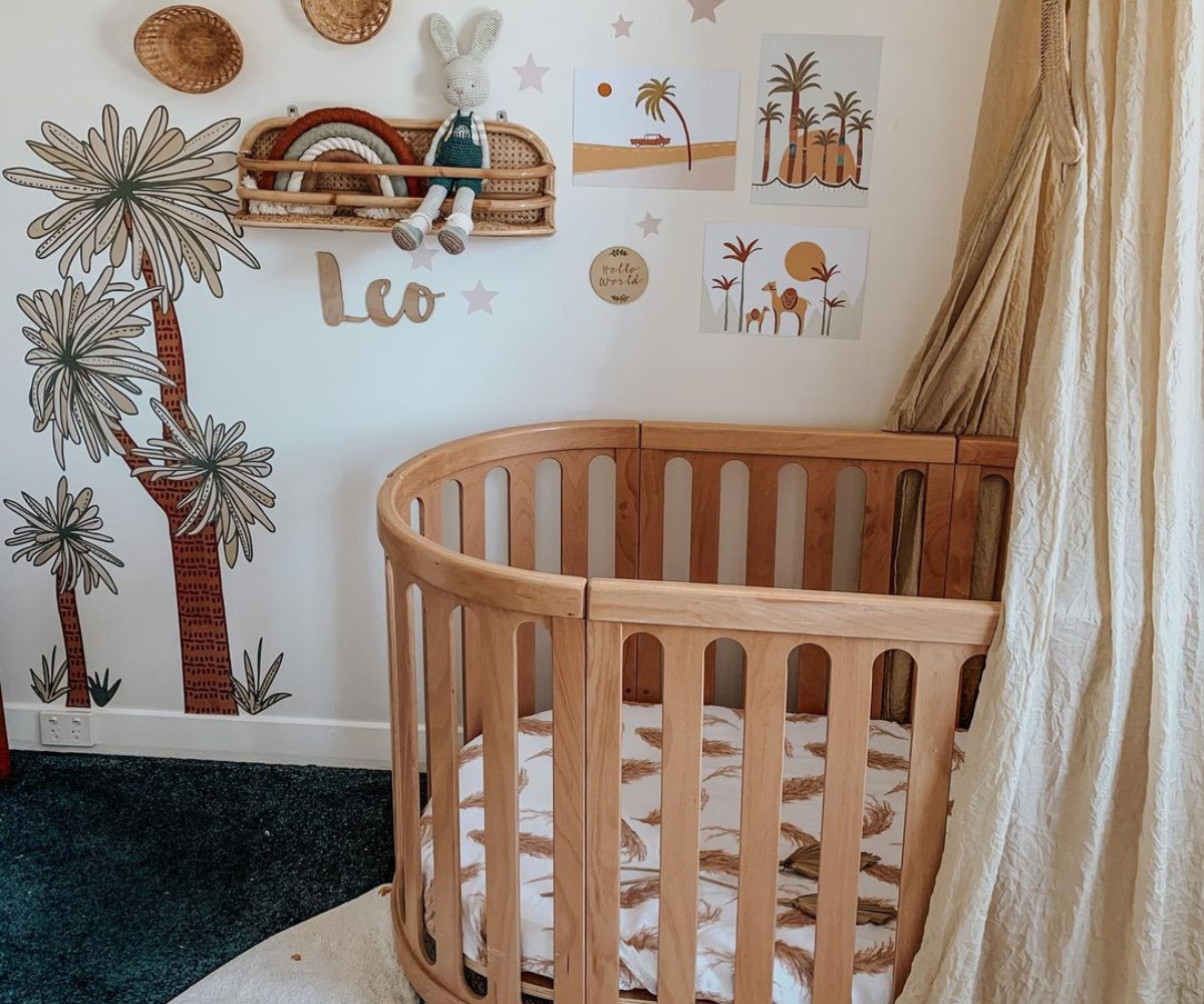 Stylish baby nursery with wooden crib, desert-themed wall art, palm tree decals, and cozy decor