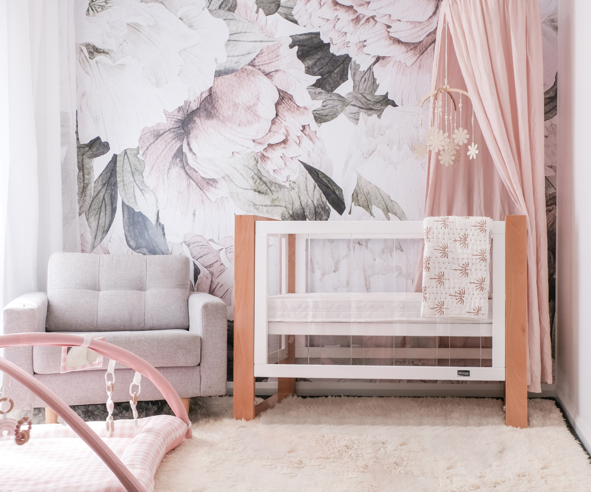 Modern baby nursery with crib, pink floral wall, armchair, play gym, and soft rug