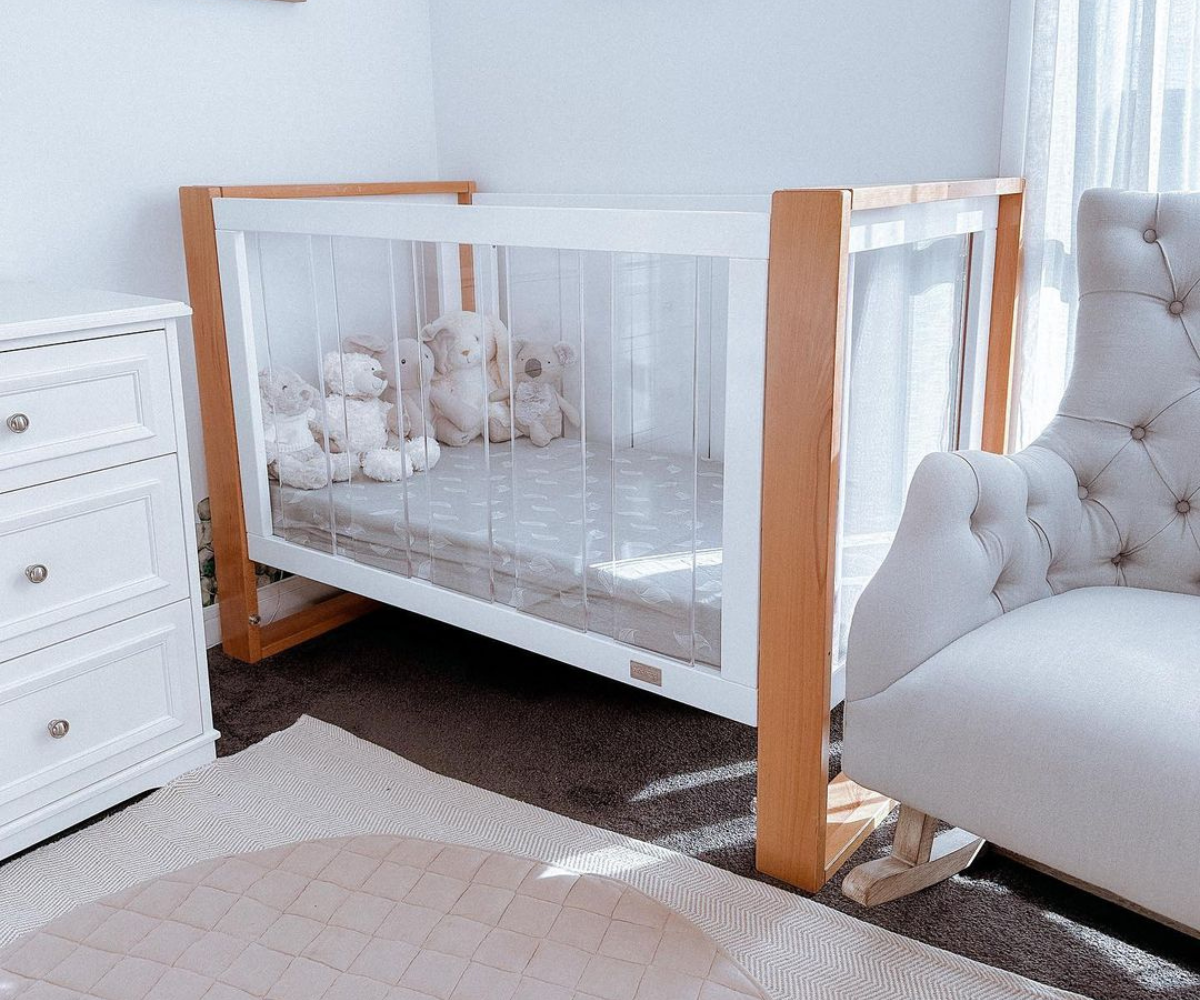 Modern baby nursery with wooden crib, plush toys, white dresser, and cozy armchair