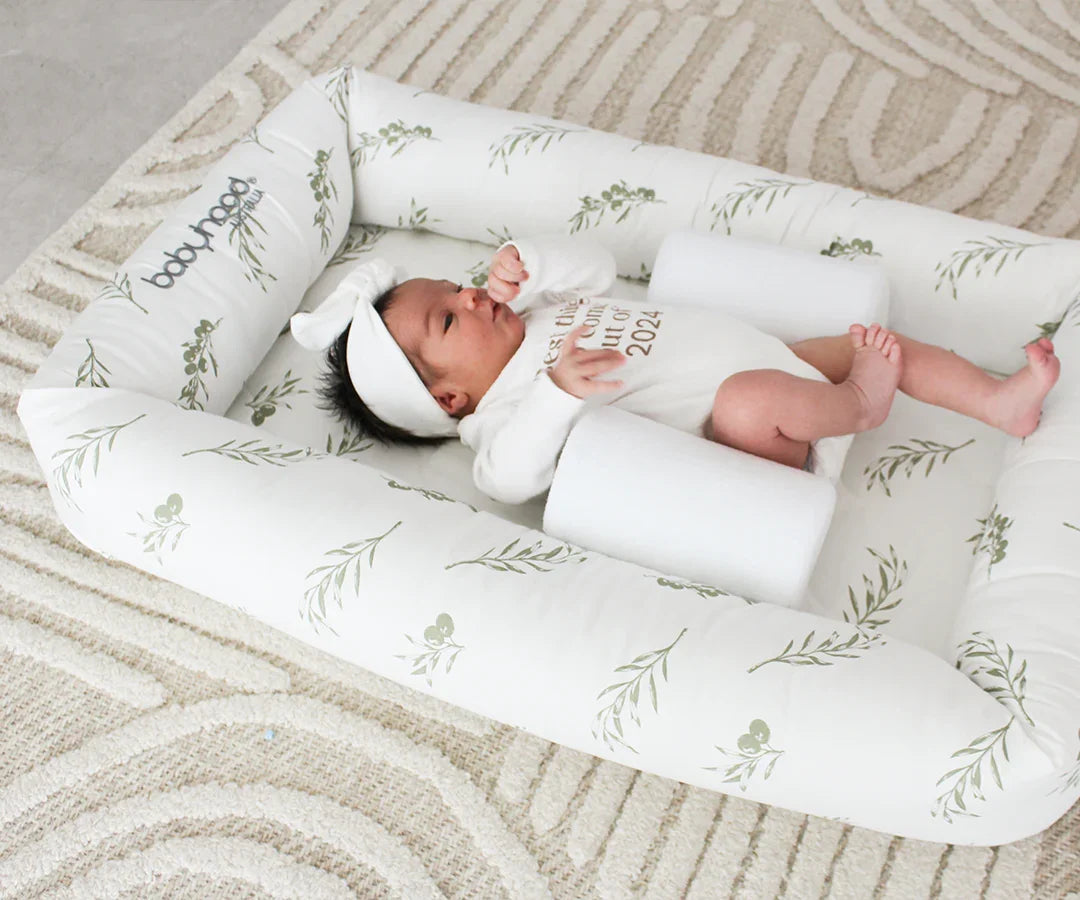 Infant lying in Babyhood Cosy Crib on patterned rug, baby sleep nest with leaf print