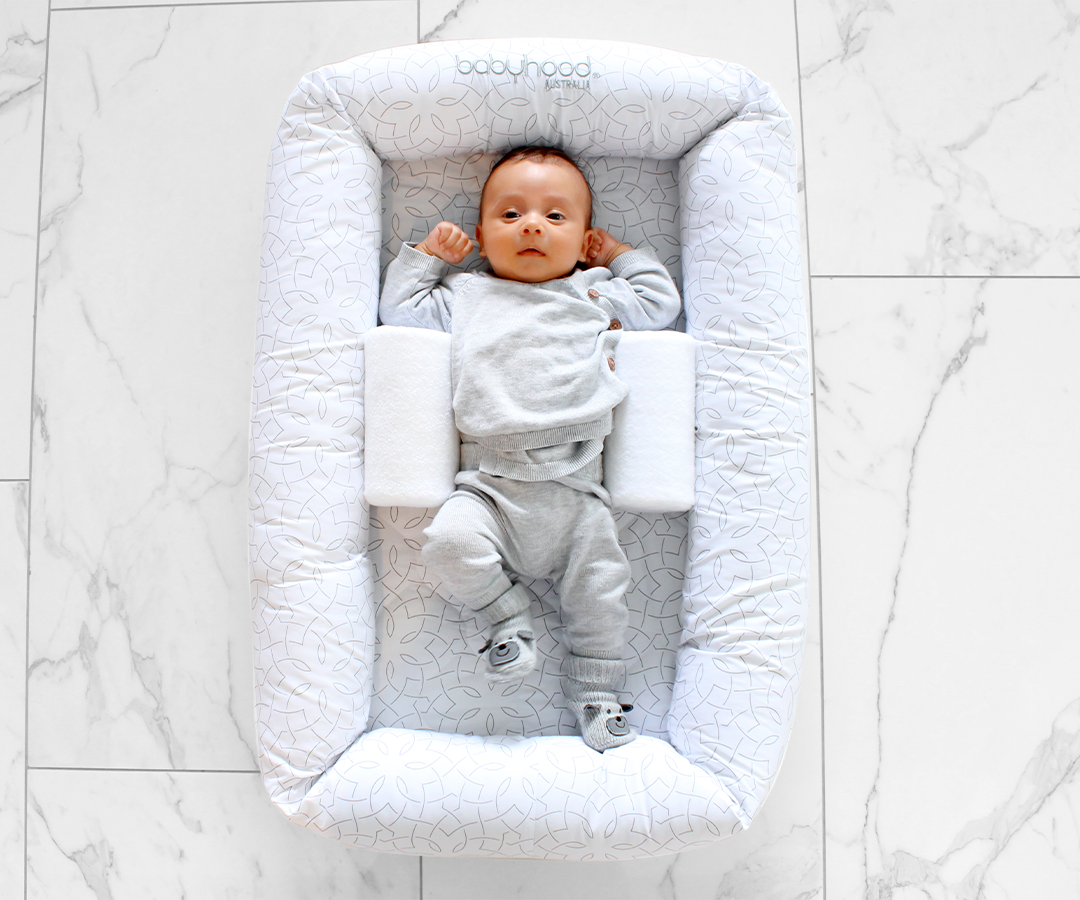 Baby in grey outfit lying in Babyhood Cosy Crib on white marble floor