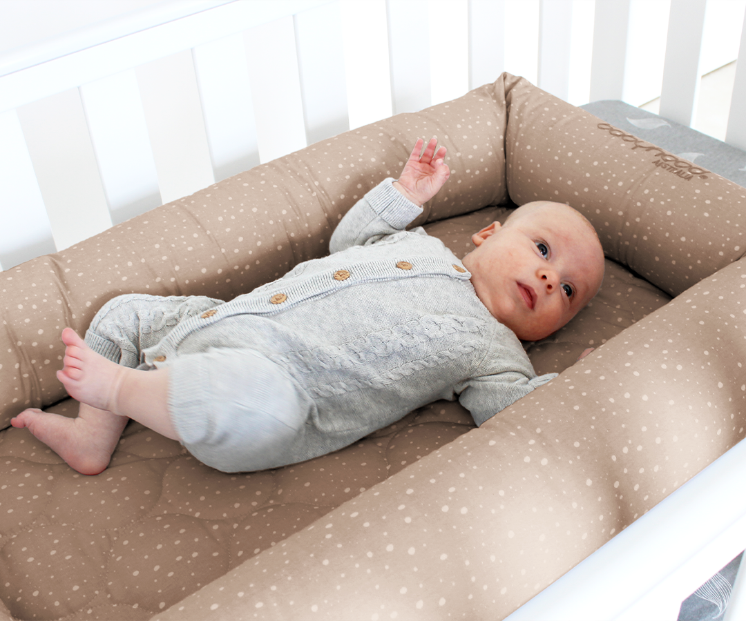 Baby lying in a beige polka dot baby nest in a white crib, Babyhood GCC product