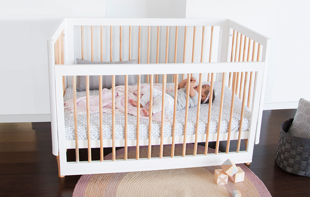 Baby lying in a modern wooden cot with white and natural bars in a nursery, Babyhood GCC
