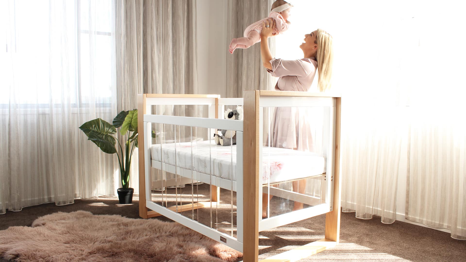 Modern baby cot in bright nursery with mother lifting baby, Babyhood GCC