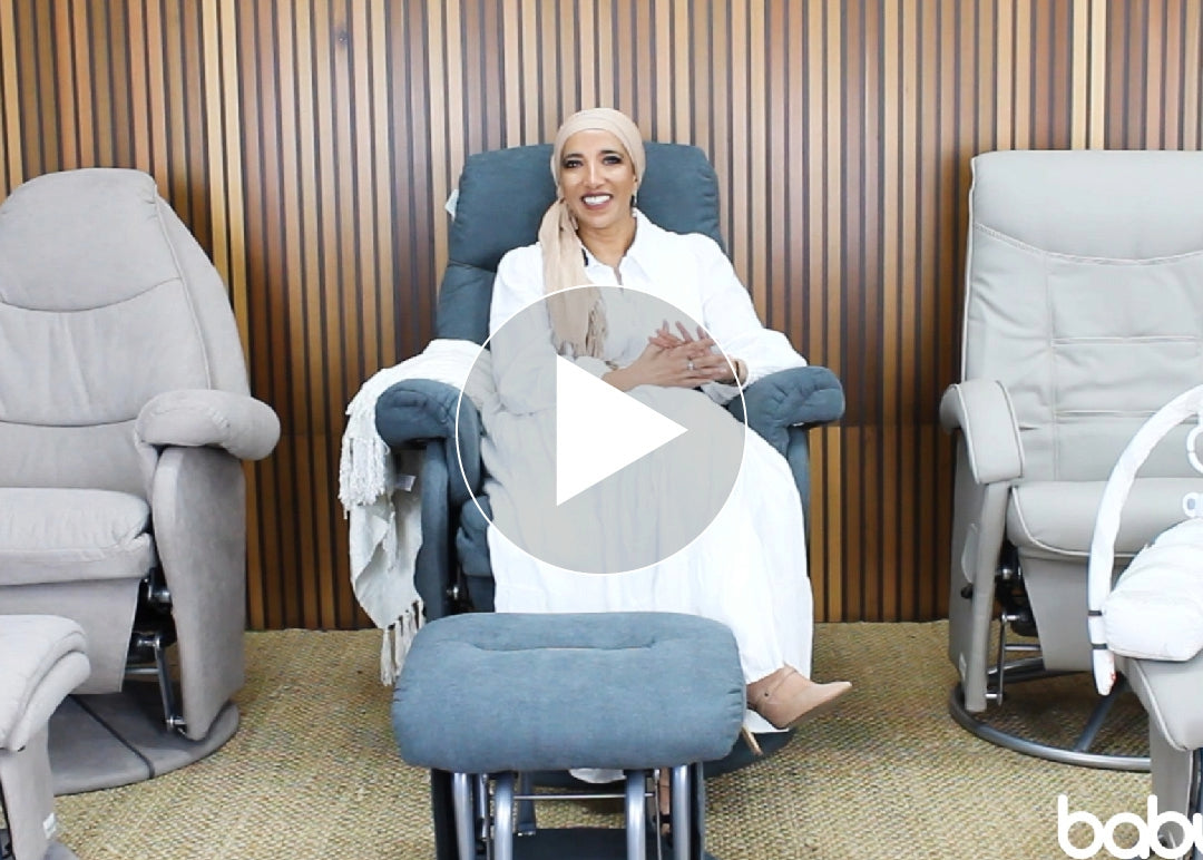 Smiling woman in white sitting on blue recliner chair, Babyhood GCC nursery furniture display