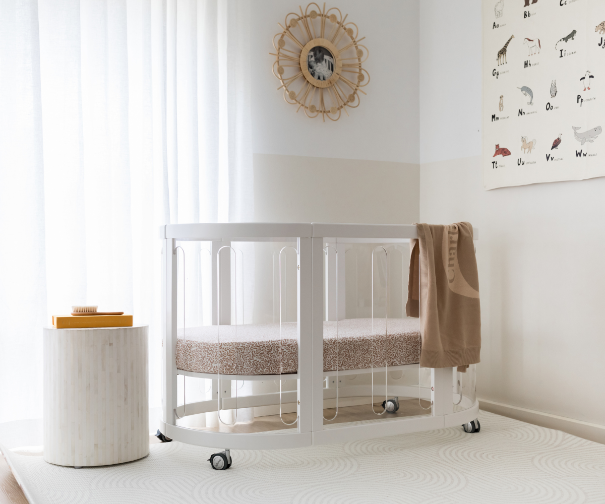 Modern white oval baby crib in sunlit nursery with alphabet wall art, Babyhood GCC