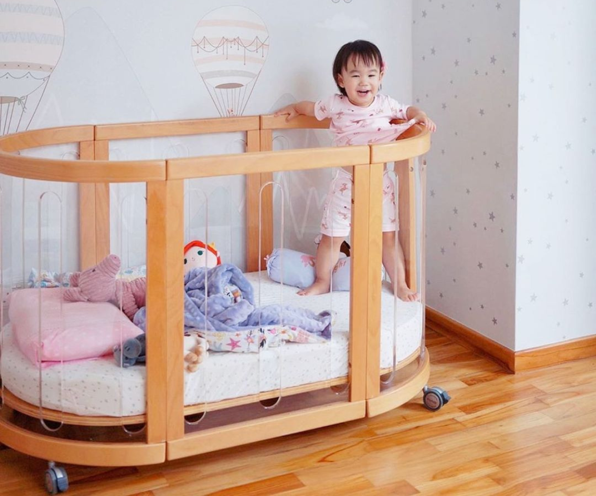 Smiling toddler in a wooden baby cot with toys, Babyhood GCC nursery setting