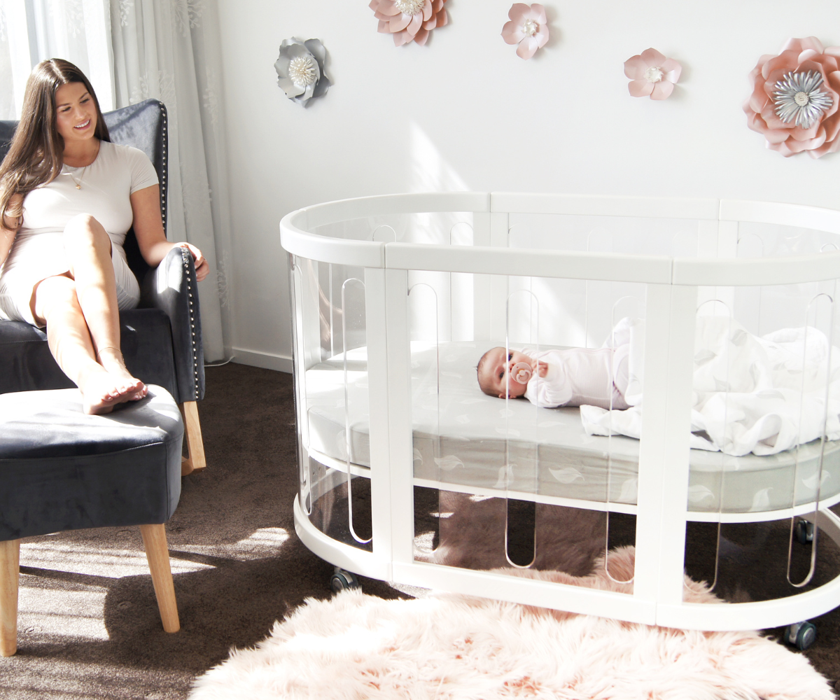 Mother sitting by modern white baby crib in a bright Babyhood GCC nursery