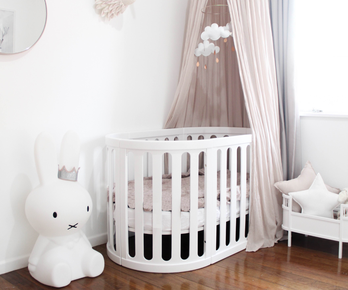 Modern white baby crib with canopy, cloud mobile, and bunny lamp in stylish nursery