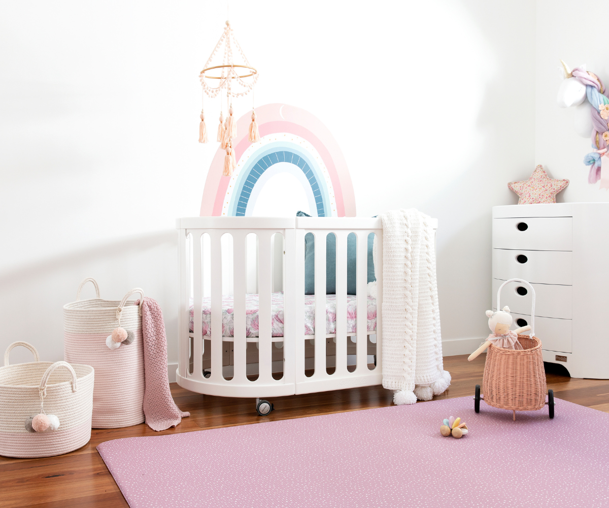 Modern baby nursery with white crib, pastel rainbow wall art, pink play mat, and storage baskets