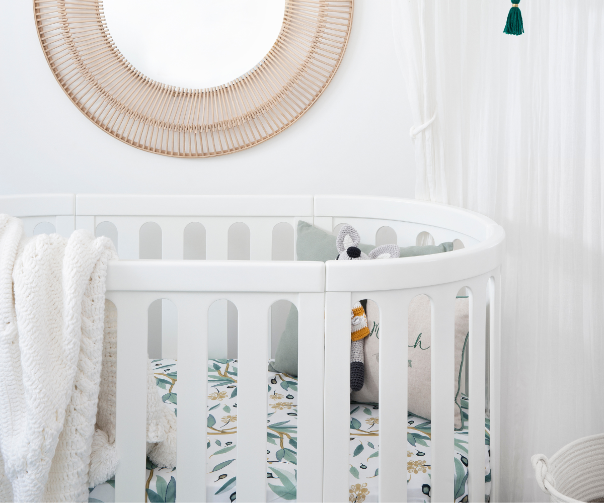 Modern white baby crib with cozy blanket, pillows, and plush toy in a bright nursery