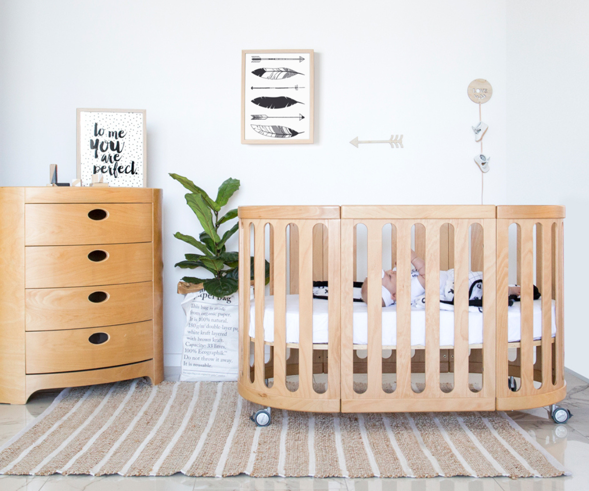 Modern natural wood baby cot in nursery with dresser, wall art, and indoor plant