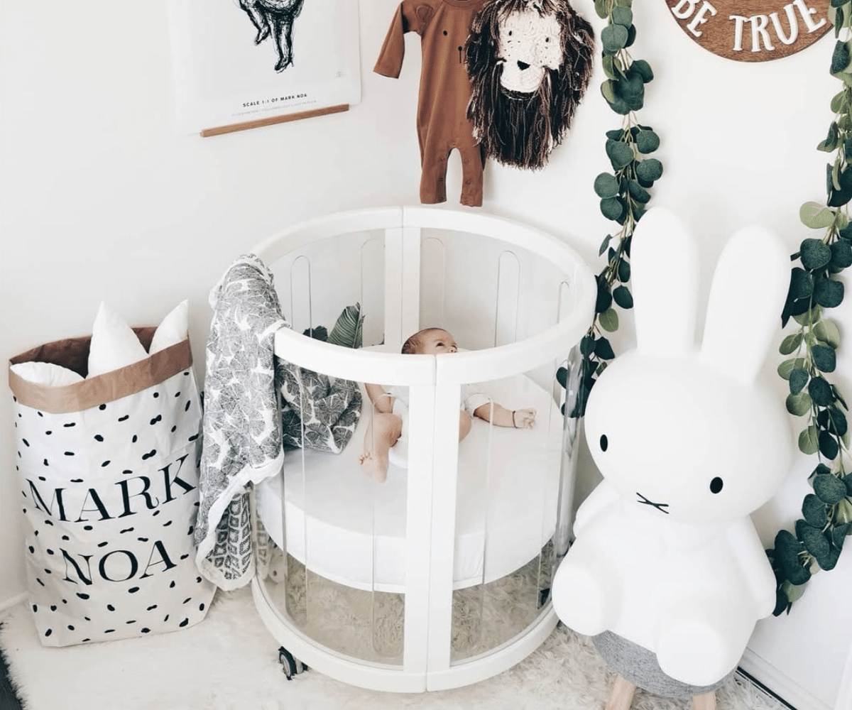 Modern baby nursery with a round white crib, baby, plush bunny, and decorative accents