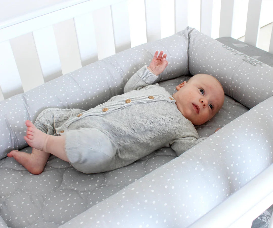 Baby in grey polka dot crib from Babyhood GCC, lying comfortably in a white cot